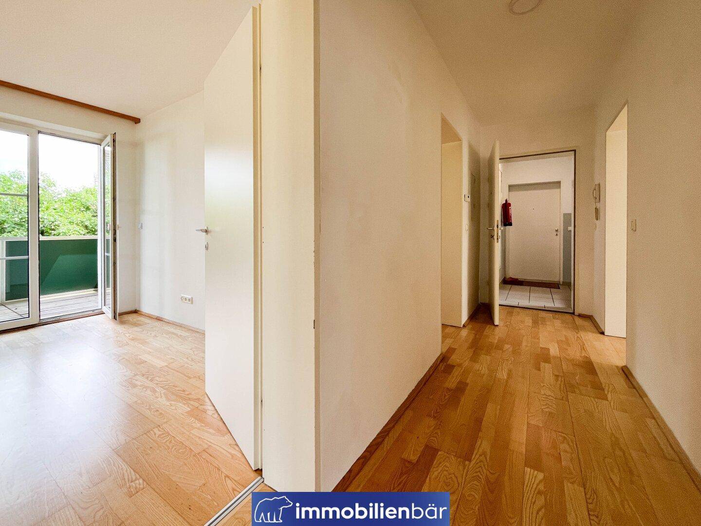 Heller Flur mit Parkettboden und Blick in ein Zimmer mit Balkonzugang.