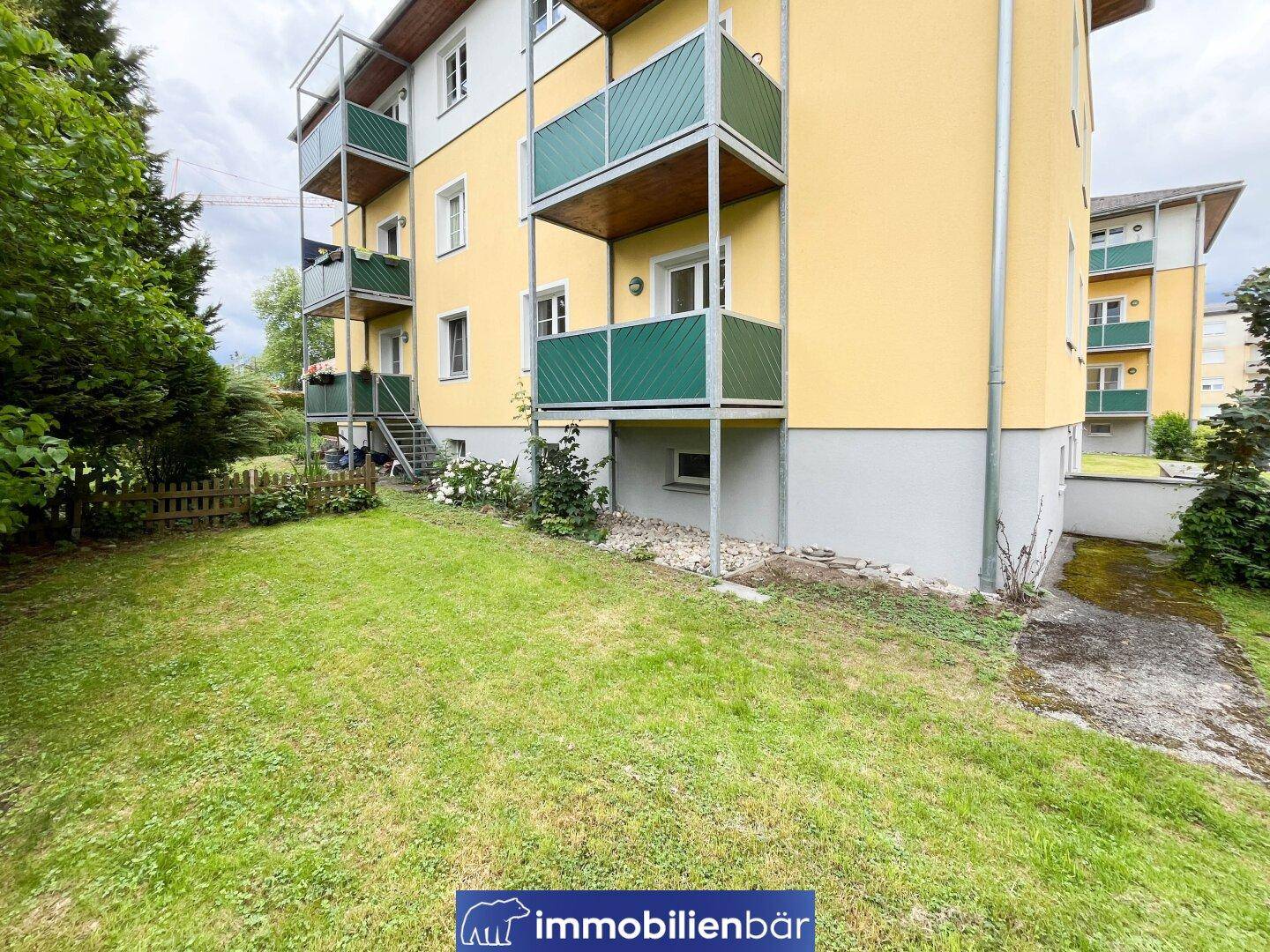 Mehrere Balkone an der gelben Fassade des Gebäudes mit angrenzender Rasenfläche.