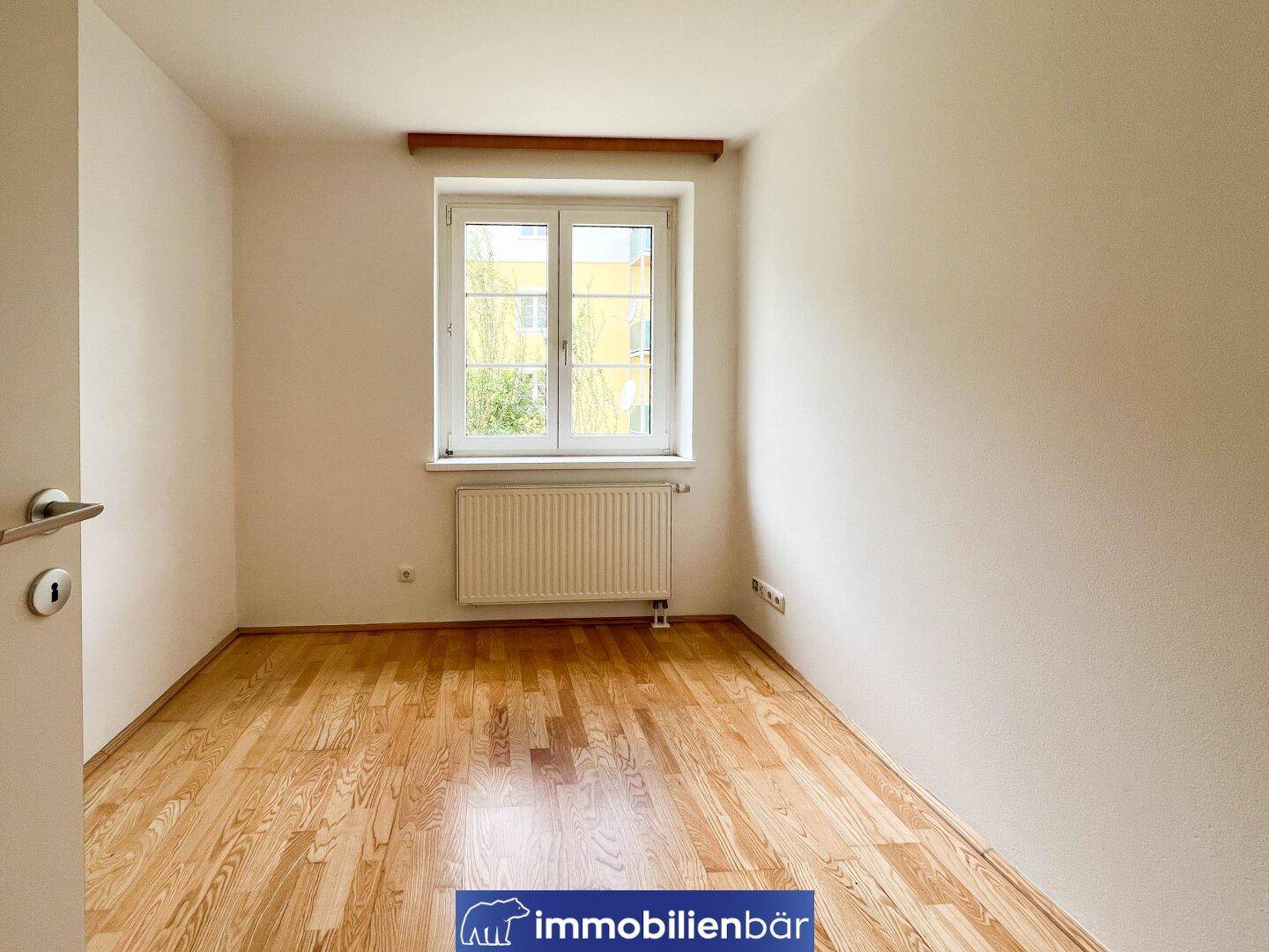Leeres Schlafzimmer mit Parkettboden, weiß gestrichenen Wänden und Heizkörper.