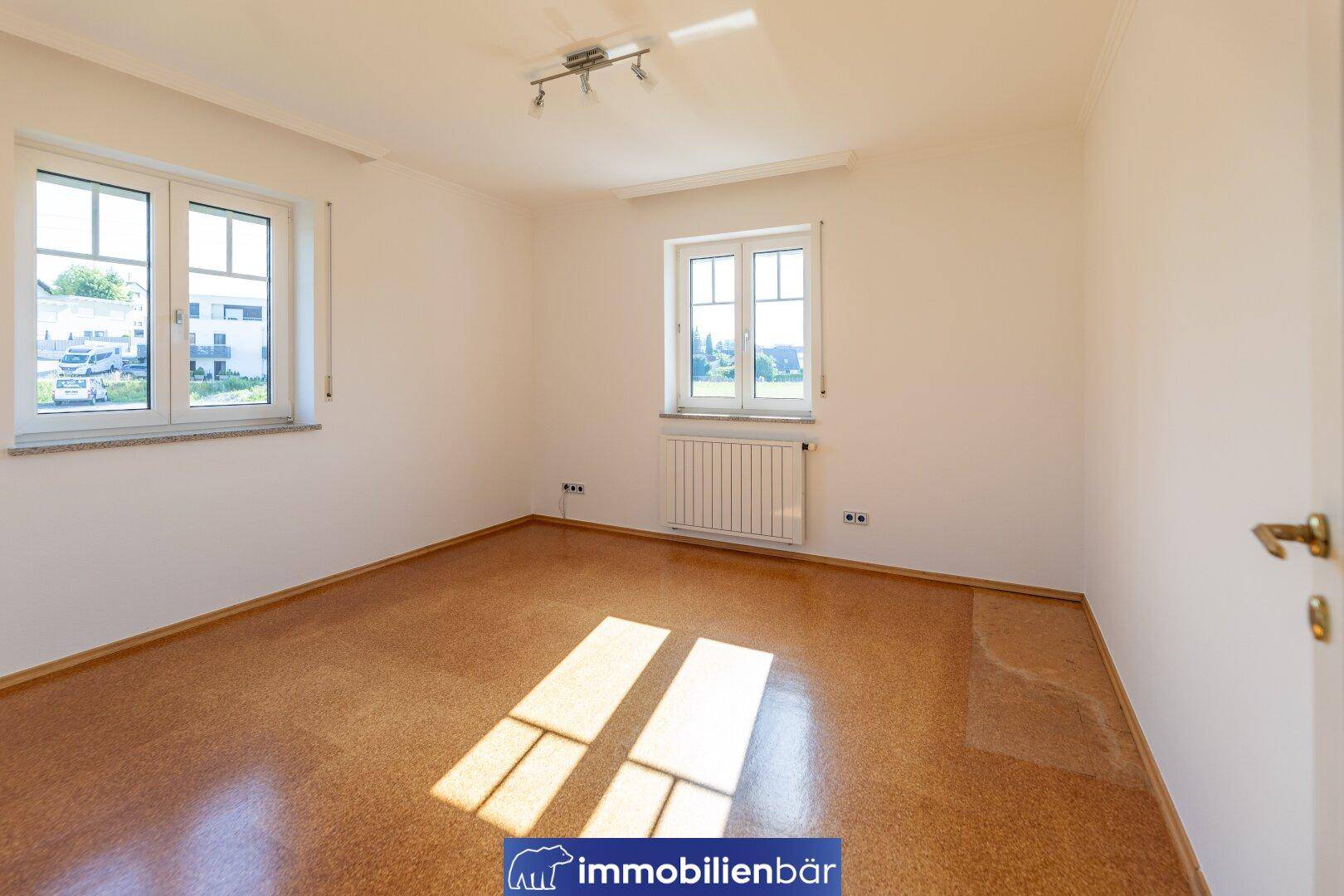 Helles Schlafzimmer mit Korkboden, zwei Fenstern und viel Tageslicht.