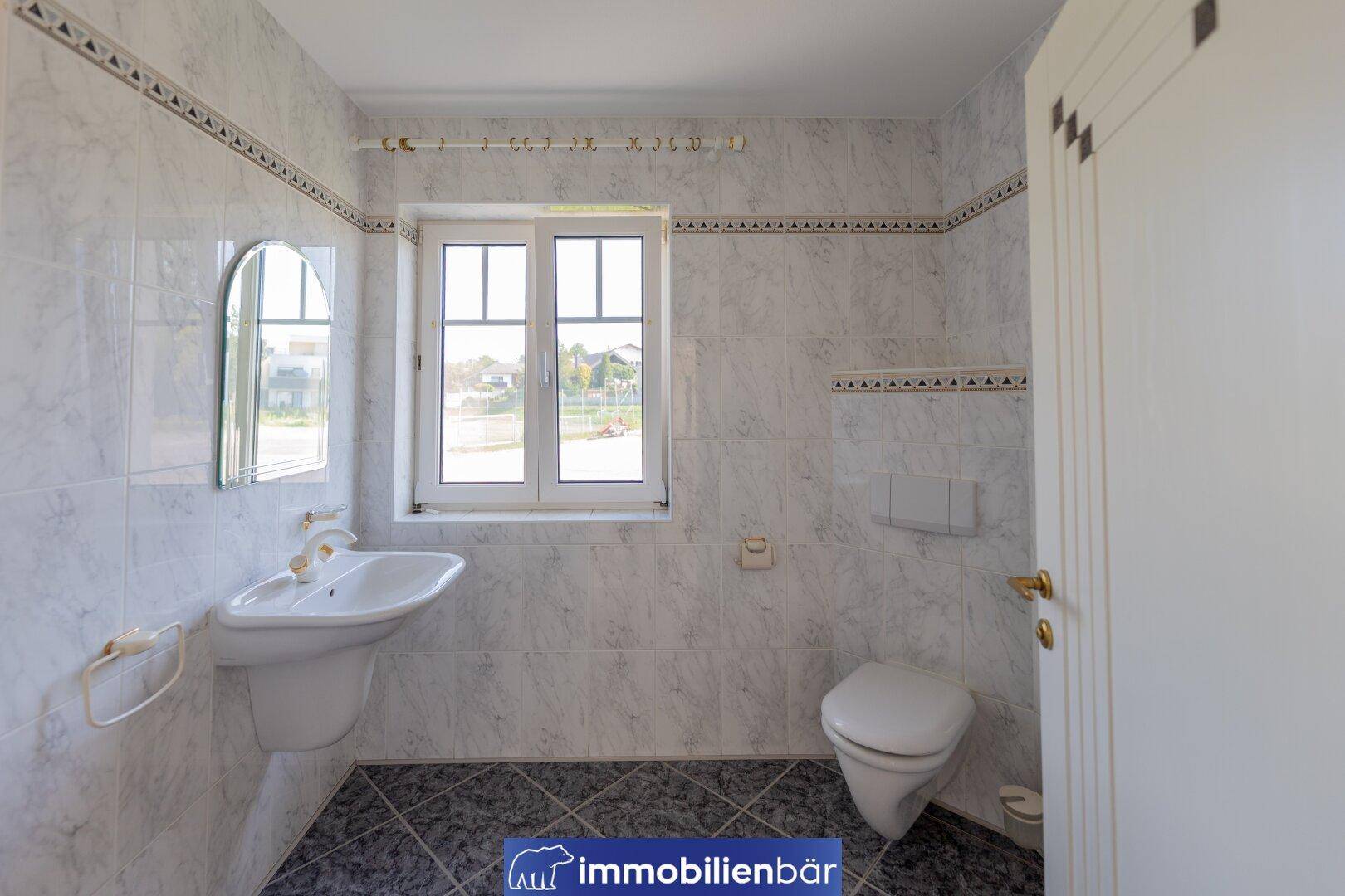 Separates WC mit Waschbecken, Fenster und hellen Fliesen.