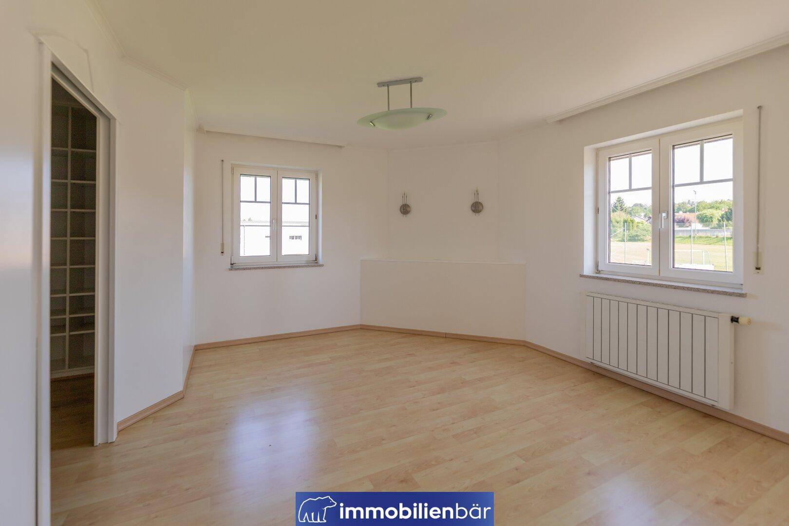 Helles Schlafzimmer mit Laminatboden, großen Fenstern und Heizkörper.