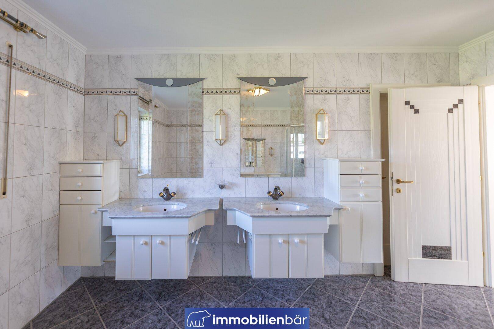 Großes Badezimmer mit Doppelwaschbecken, Marmoroberflächen und hellen Fliesen.