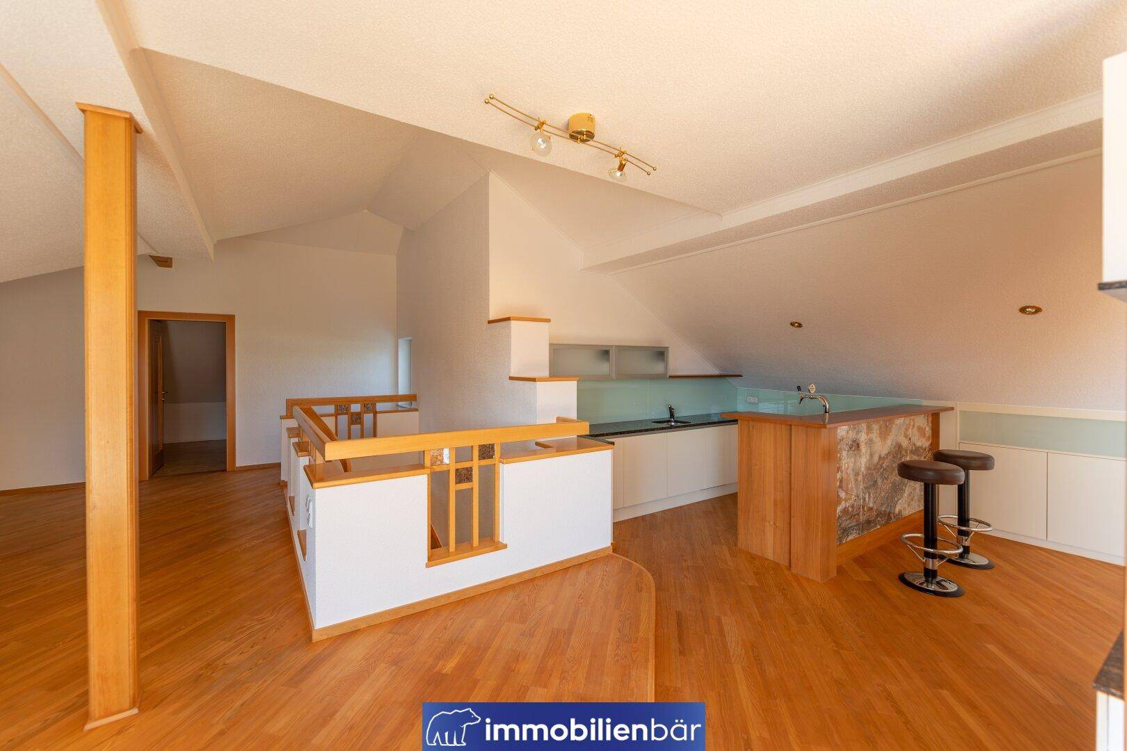 Heller, offener Wohnbereich im Dachgeschoss mit Holzboden und integrierter Bar, ideal für geselliges Beisammensein.