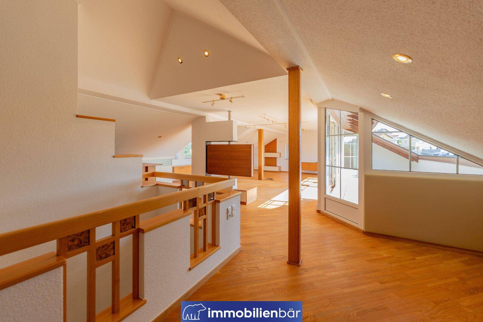 Weitläufiger Wohnbereich im Dachgeschoss mit Holzboden, viel Tageslicht und Blick auf die Umgebung.