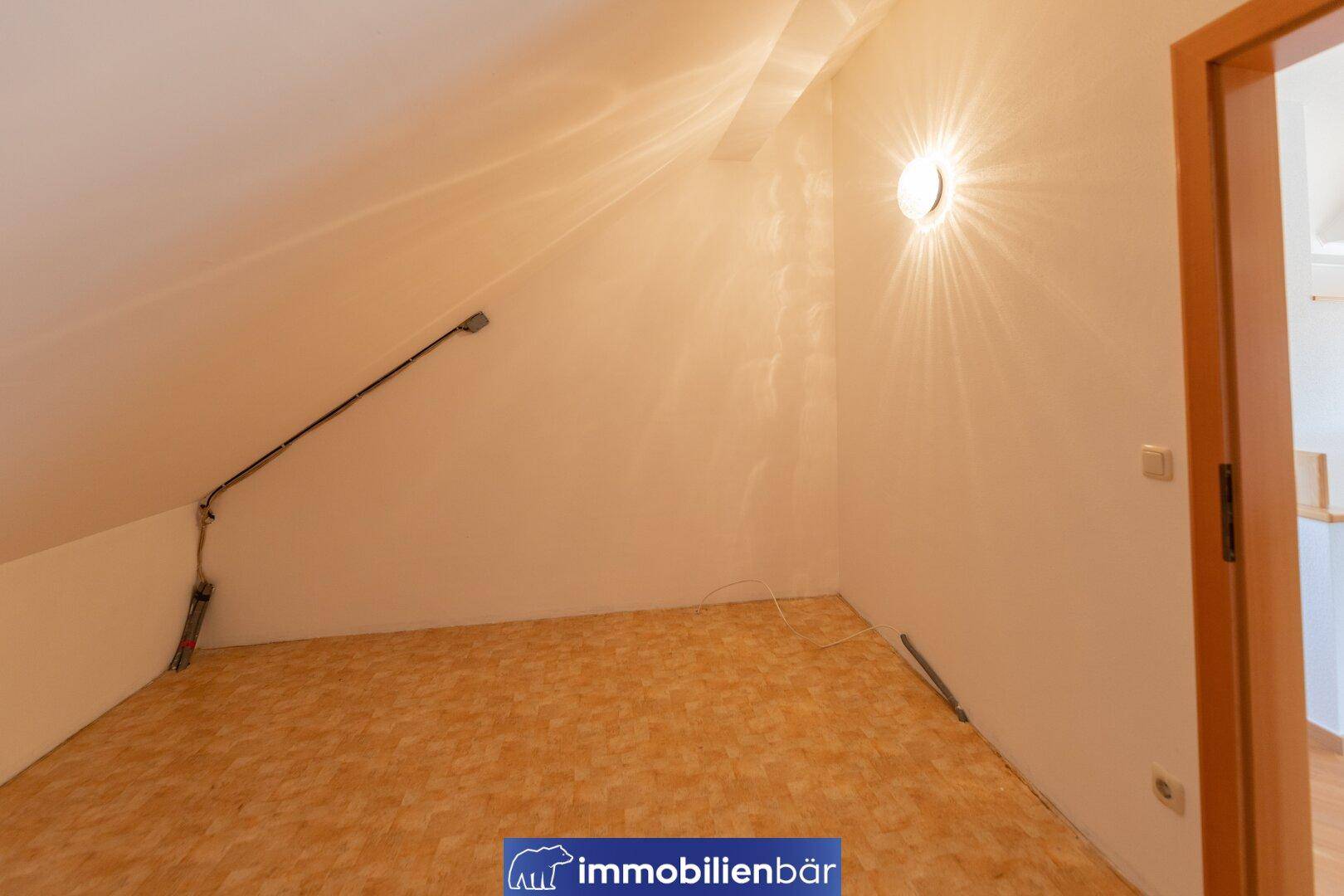 Kleiner Raum im Dachgeschoss mit Schrägen und einfacher Beleuchtung, ideal als Schlaf- oder Arbeitszimmer.