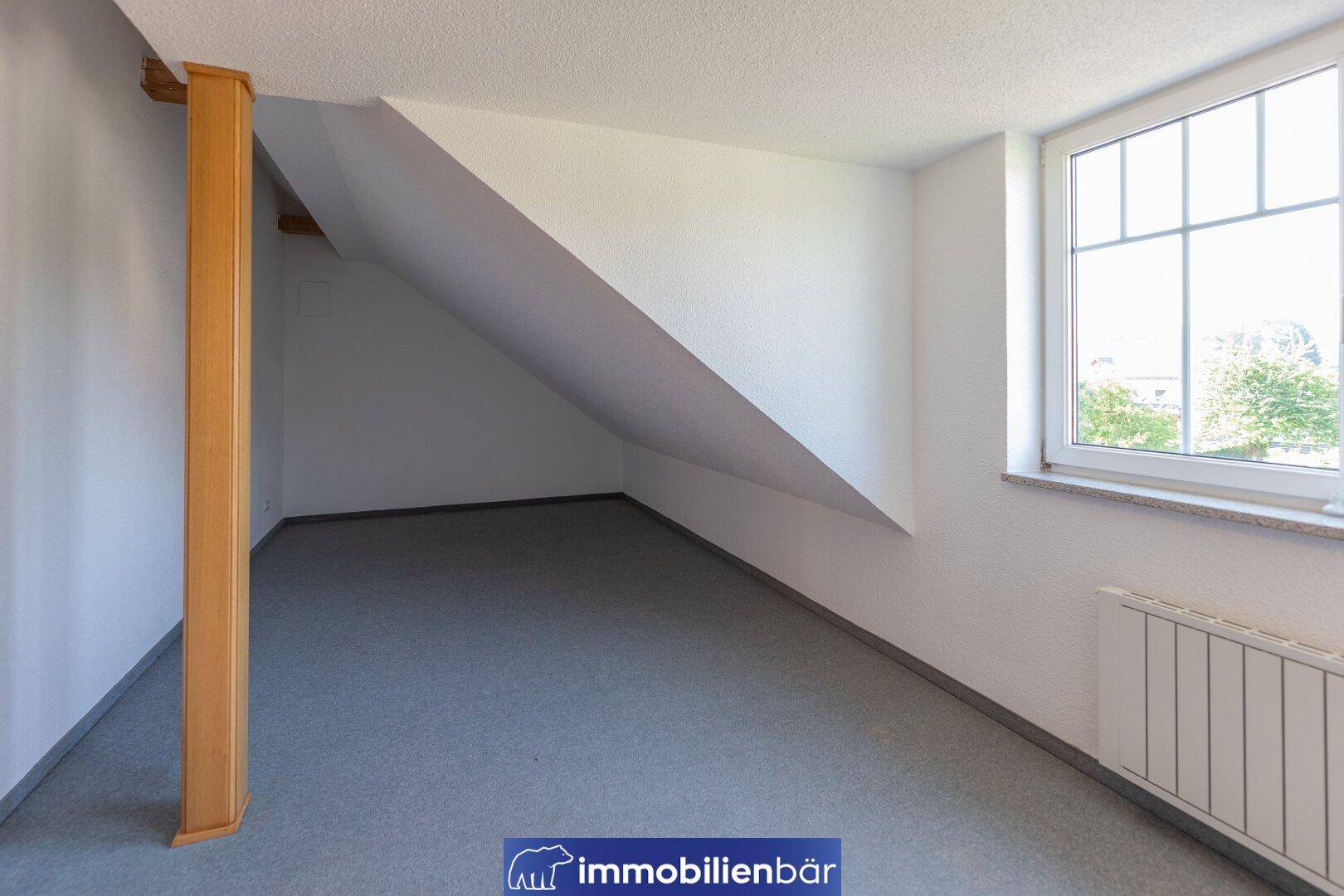 Helles Zimmer im Dachgeschoss mit Schrägen, Fenster und Heizkörper, ausgestattet mit Teppichboden.