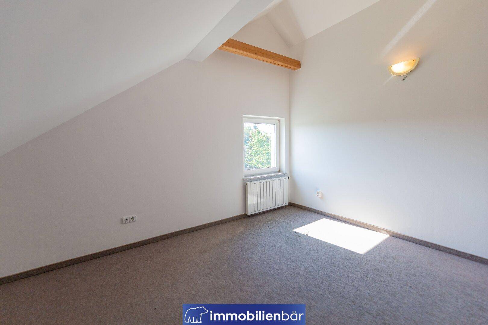 Ruhiges Zimmer im Dachgeschoss mit Schrägen, einem Fenster und Teppichboden, bietet viel Tageslicht.