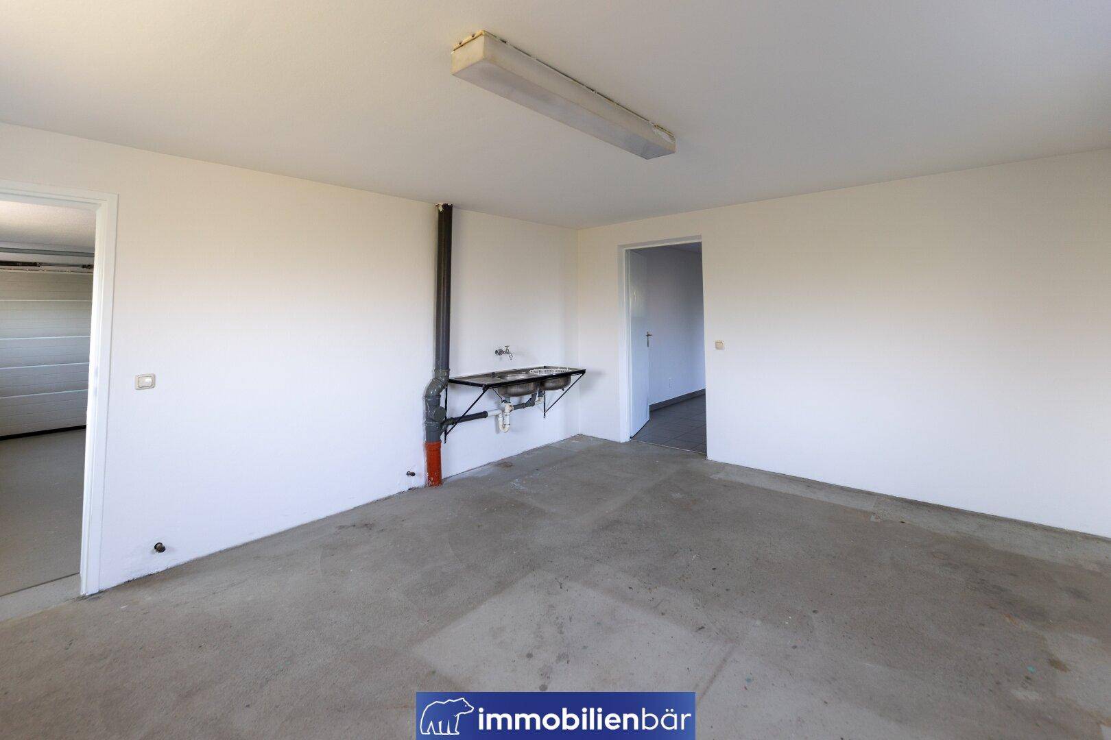 Funktionaler Raum mit Waschbecken und Zugang zur Garage, geeignet als Werkstatt oder Lager.