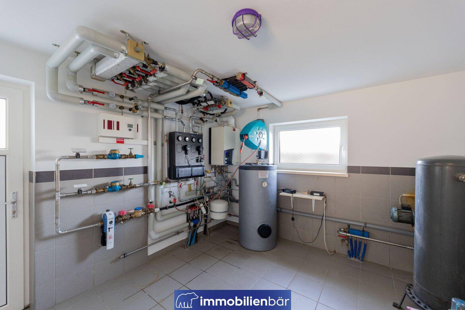 Heizungsraum mit komplexen Rohrleitungen, Warmwasserspeicher und Fenster, gut organisiert und funktional.