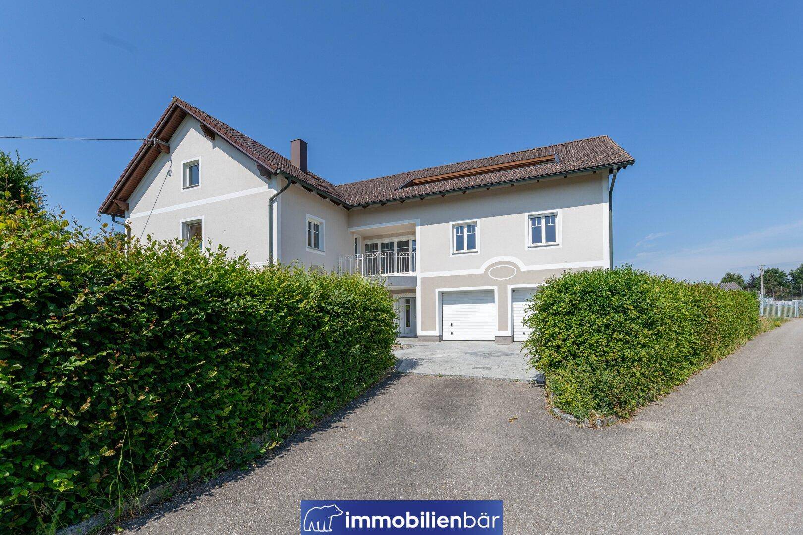 Ansicht des Hauses von der Zufahrt aus, umgeben von hohen Hecken und gepflegtem Rasen.