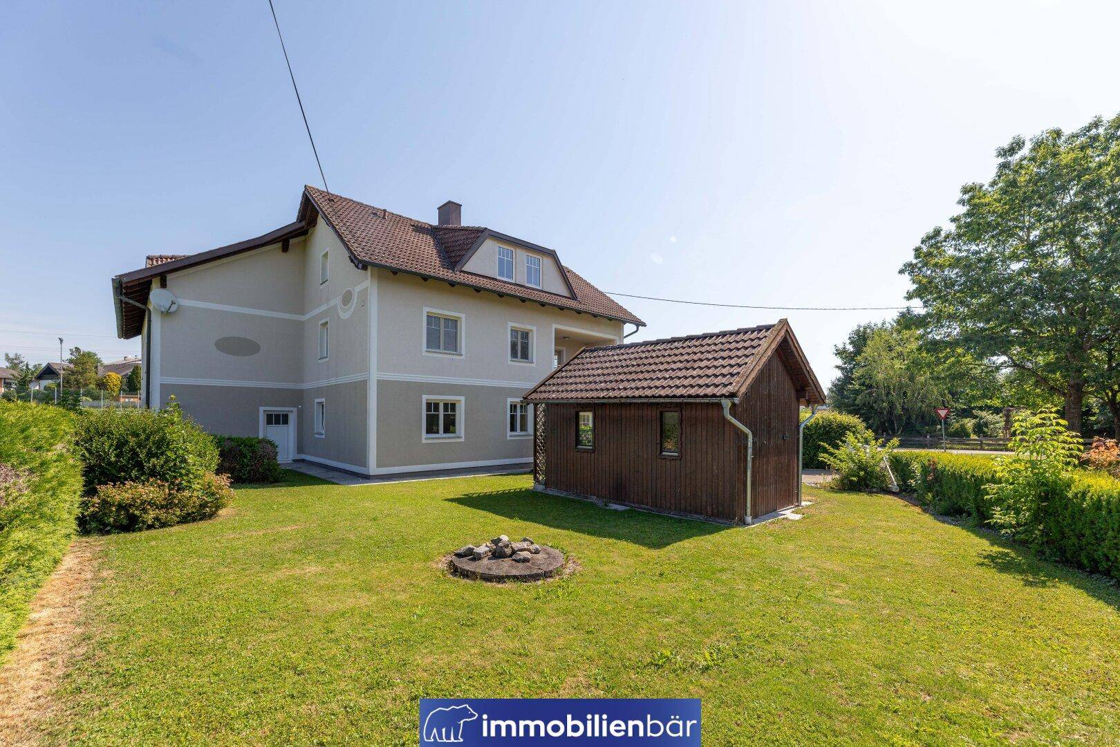 Gepflegter Gartenbereich mit Rasenfläche, Feuerstelle und einem kleinen Holzschuppen neben dem Haus.