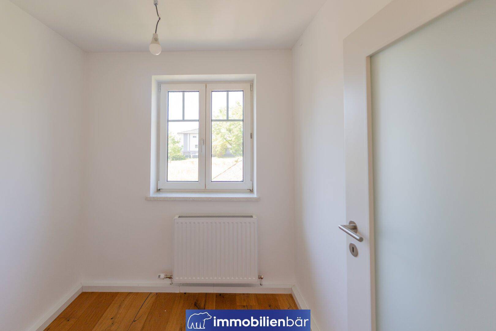 Kleinerer, heller Raum mit Holzboden, weiß gestrichenen Wänden und einem Fenster.