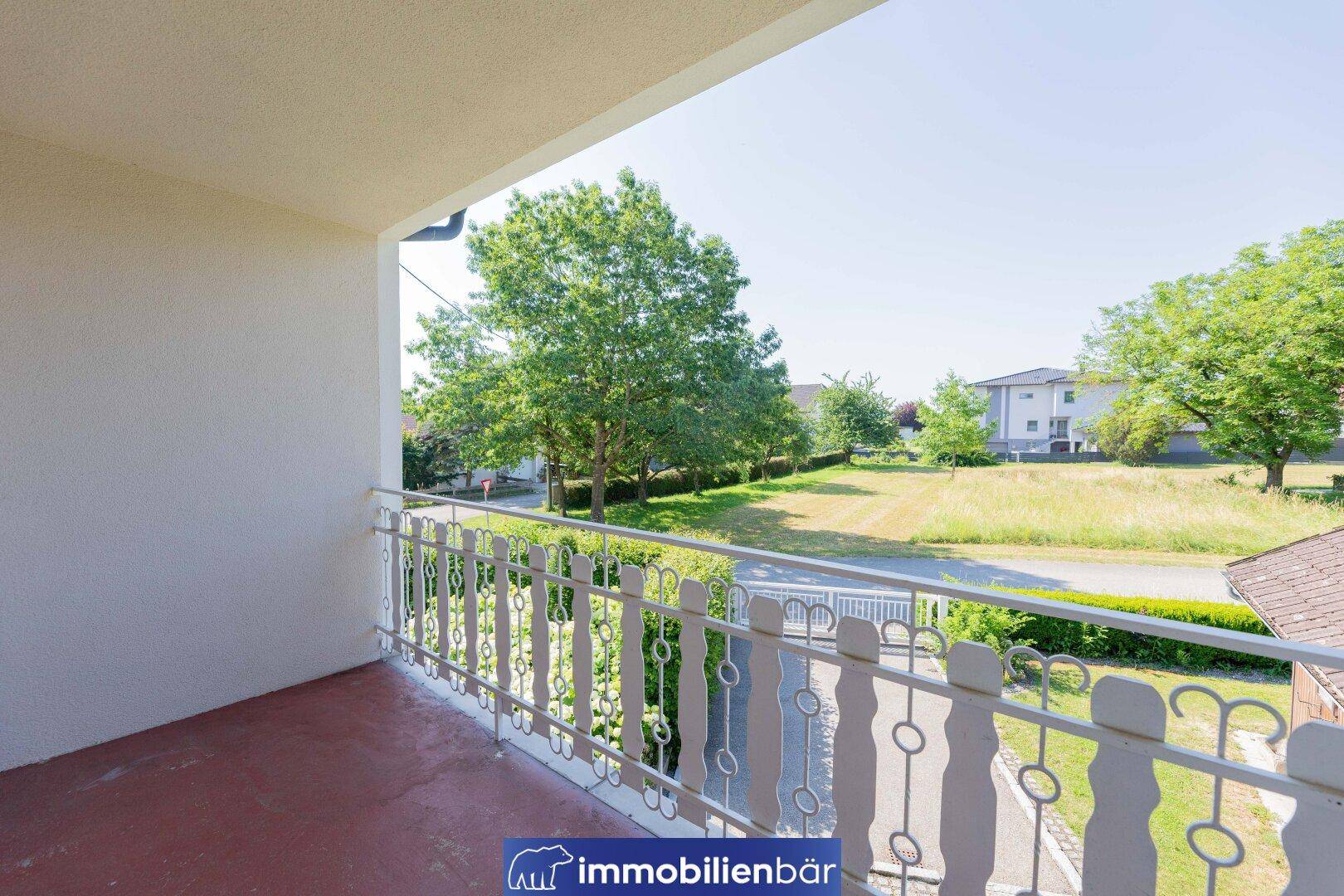 Balkon mit weißem Geländer und Blick auf die grüne Umgebung und Bäume.