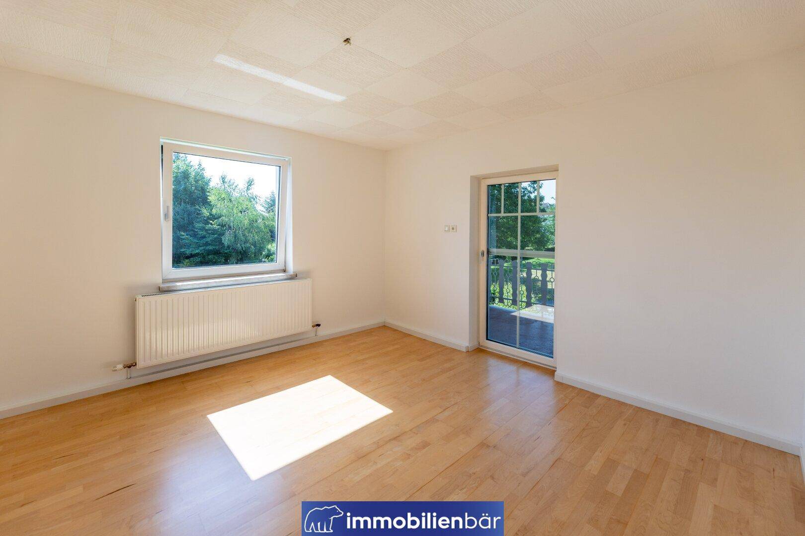 Heller Raum mit Holzboden, großem Fenster und Zugang zu einem Außenbereich.