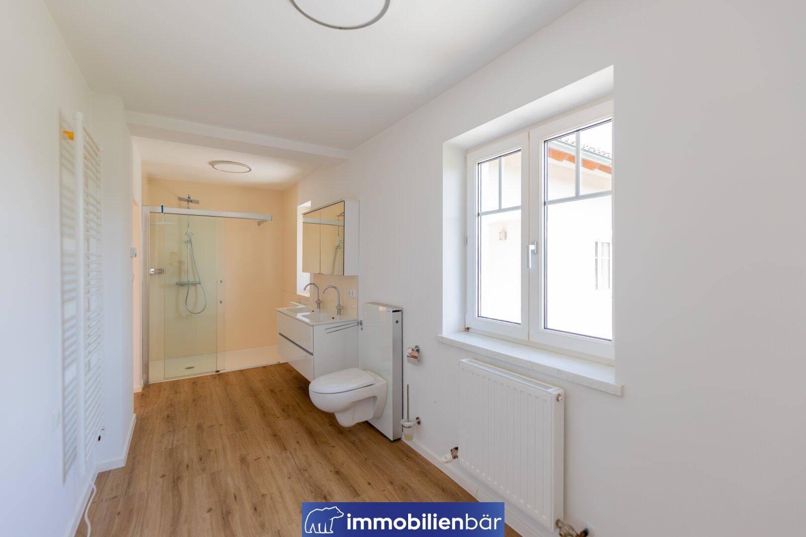 Modernes Badezimmer mit Dusche, wandhängendem WC, Doppelwaschbecken und Fenster.