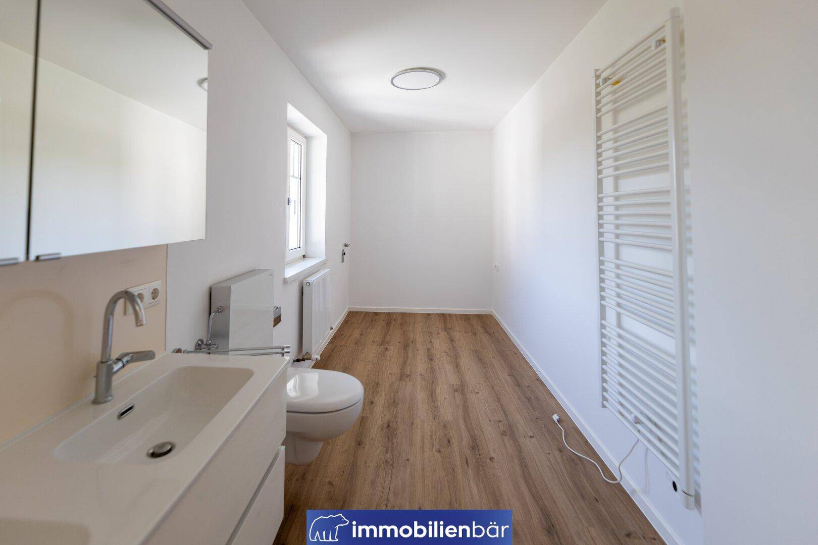 Helles Badezimmer mit Einzelwaschbecken, WC, Spiegelschrank und beheiztem Handtuchhalter.