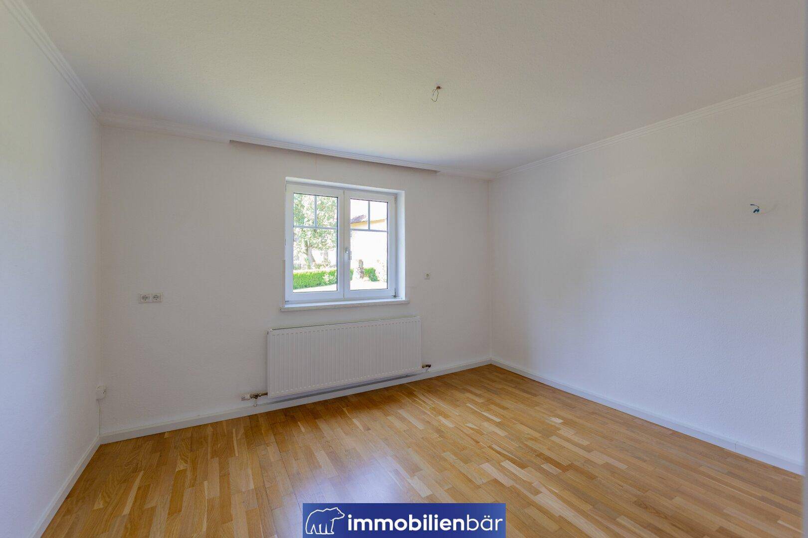 Helles Schlafzimmer mit Holzboden, weiß gestrichenen Wänden und einem Fenster.