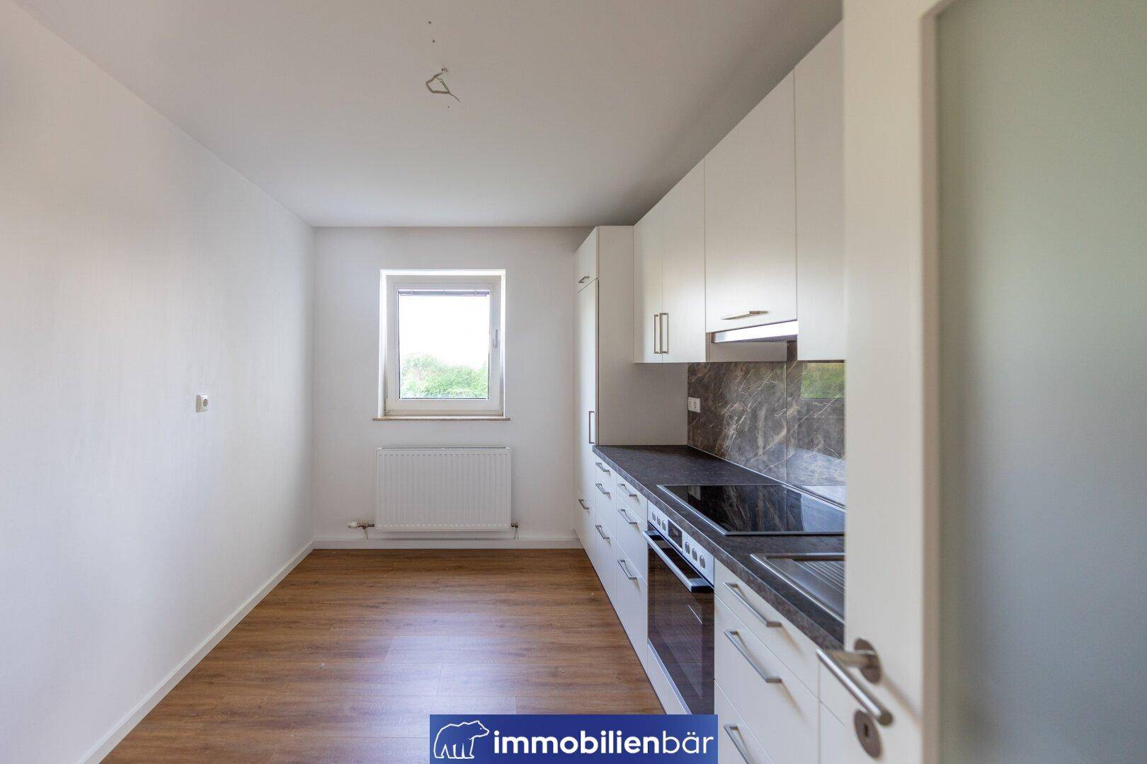 Moderne, unmöblierte Küche mit weißen Schränken, dunkler Arbeitsplatte und Fenster.