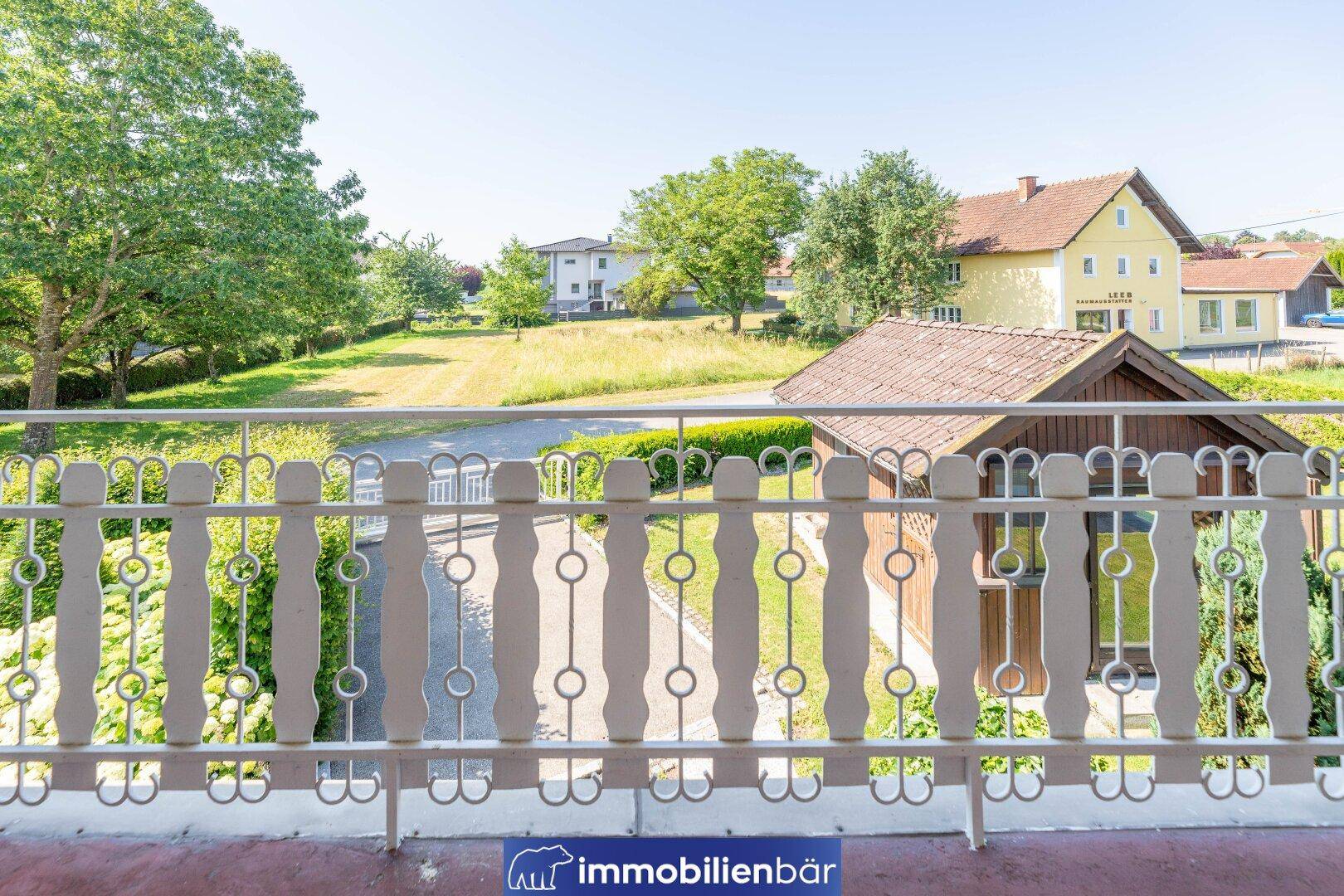Balkon mit weißem Geländer und weitem Blick auf die grüne Landschaft und Nachbarhäuser.
