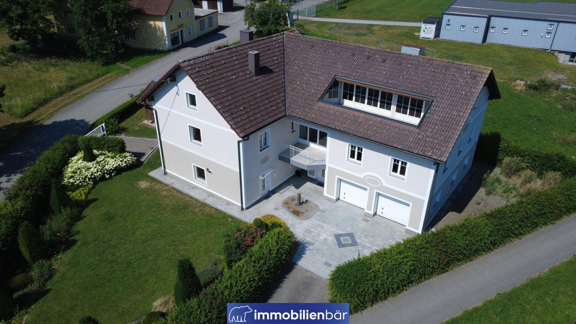Vogelperspektive des Hauses mit Doppelgarage, gepflasterter Einfahrt und umliegendem Grünbereich.