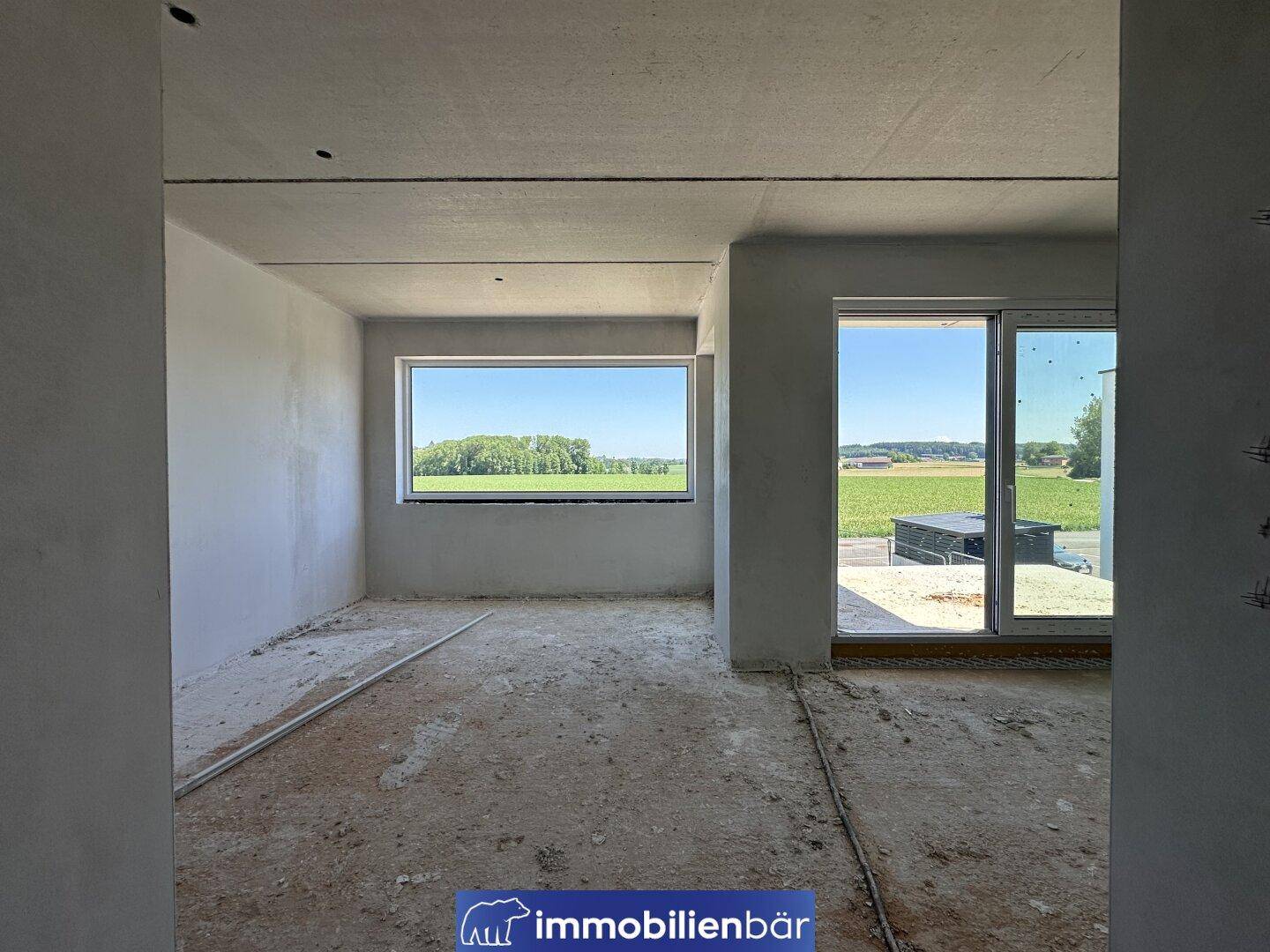 Unfertiger Innenraum mit Blick auf die grüne Landschaft durch große Fenster.