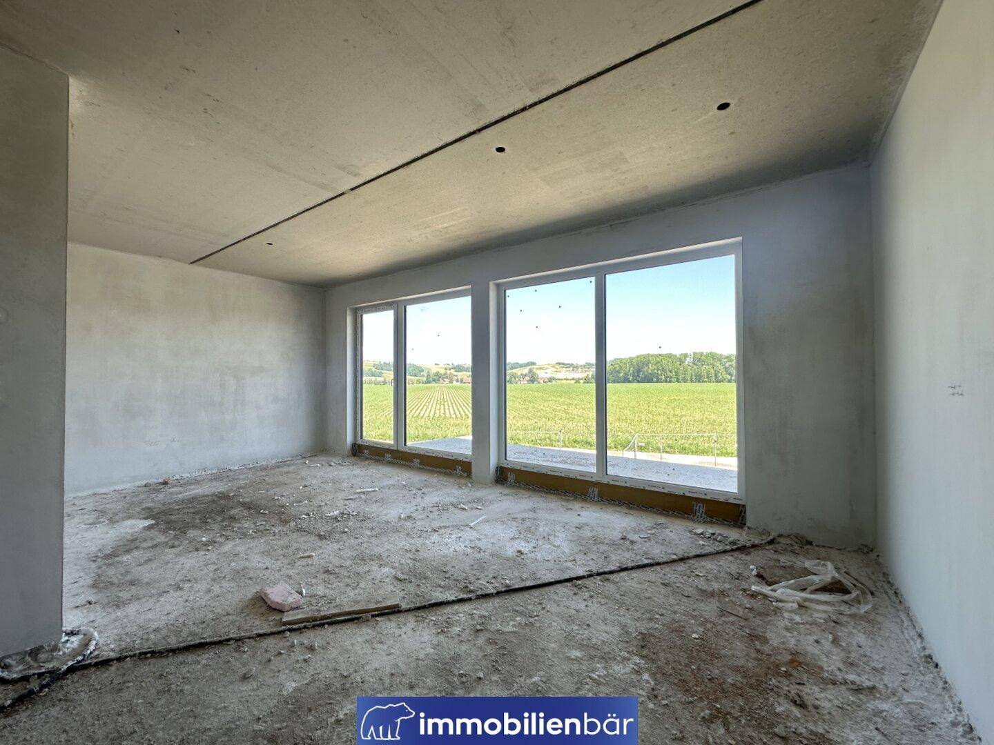 Heller Rohbau-Raum mit weitem Blick über Felder durch bodentiefe Fenster.