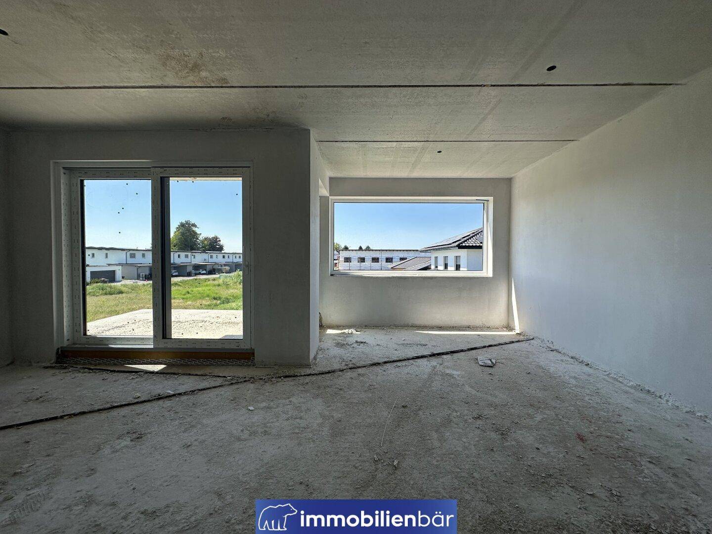 Rohbau-Zimmer mit zwei großen Fenstern und Ausblick auf die Umgebung.