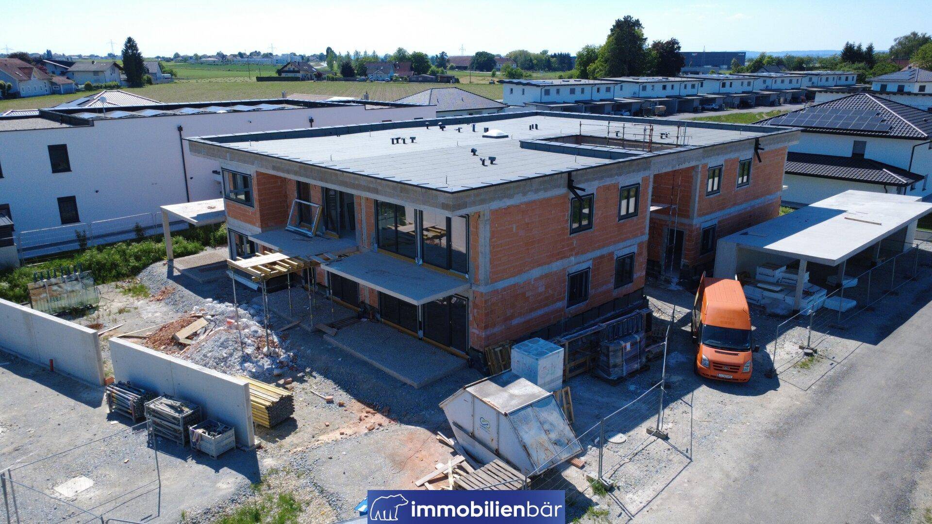 Seitenansicht des Neubaus im Rohbau mit Flachdach und angrenzender Baustelle.