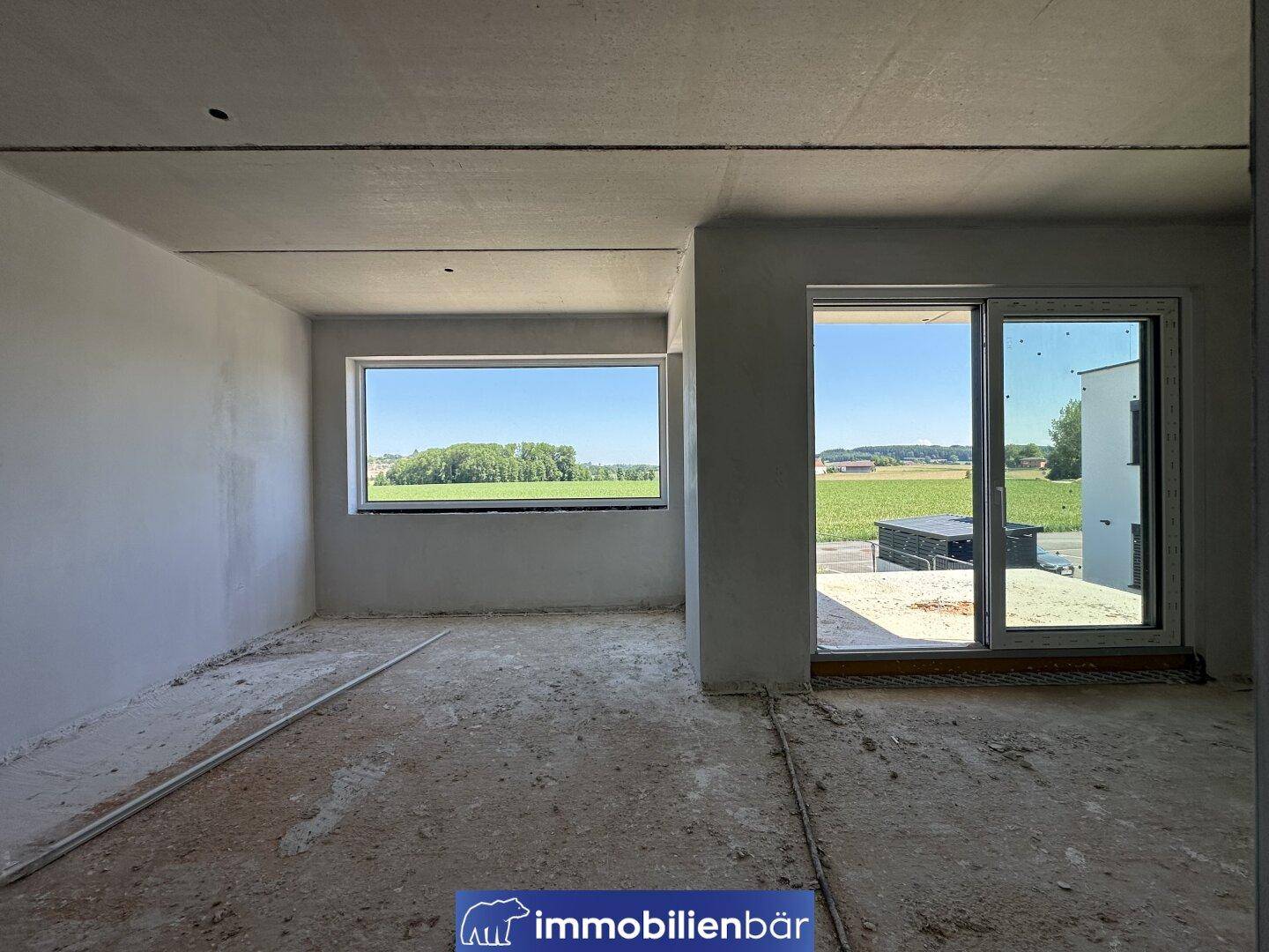 Heller Innenraum im Rohbau mit großen Fenstern und weitem Blick ins Grüne, bereit für den Ausbau.