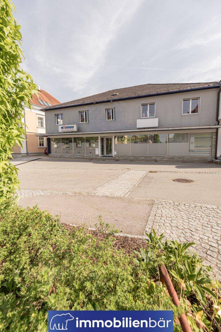 Fassade eines Geschäftsgebäudes mit großen Fenstern und gepflastertem Vorplatz.