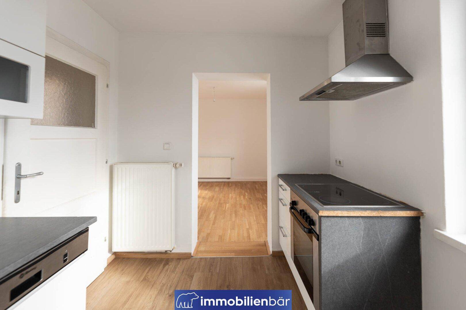 Funktionale Küche mit Herd, Backofen und Dunstabzugshaube, offen zum angrenzenden Zimmer.