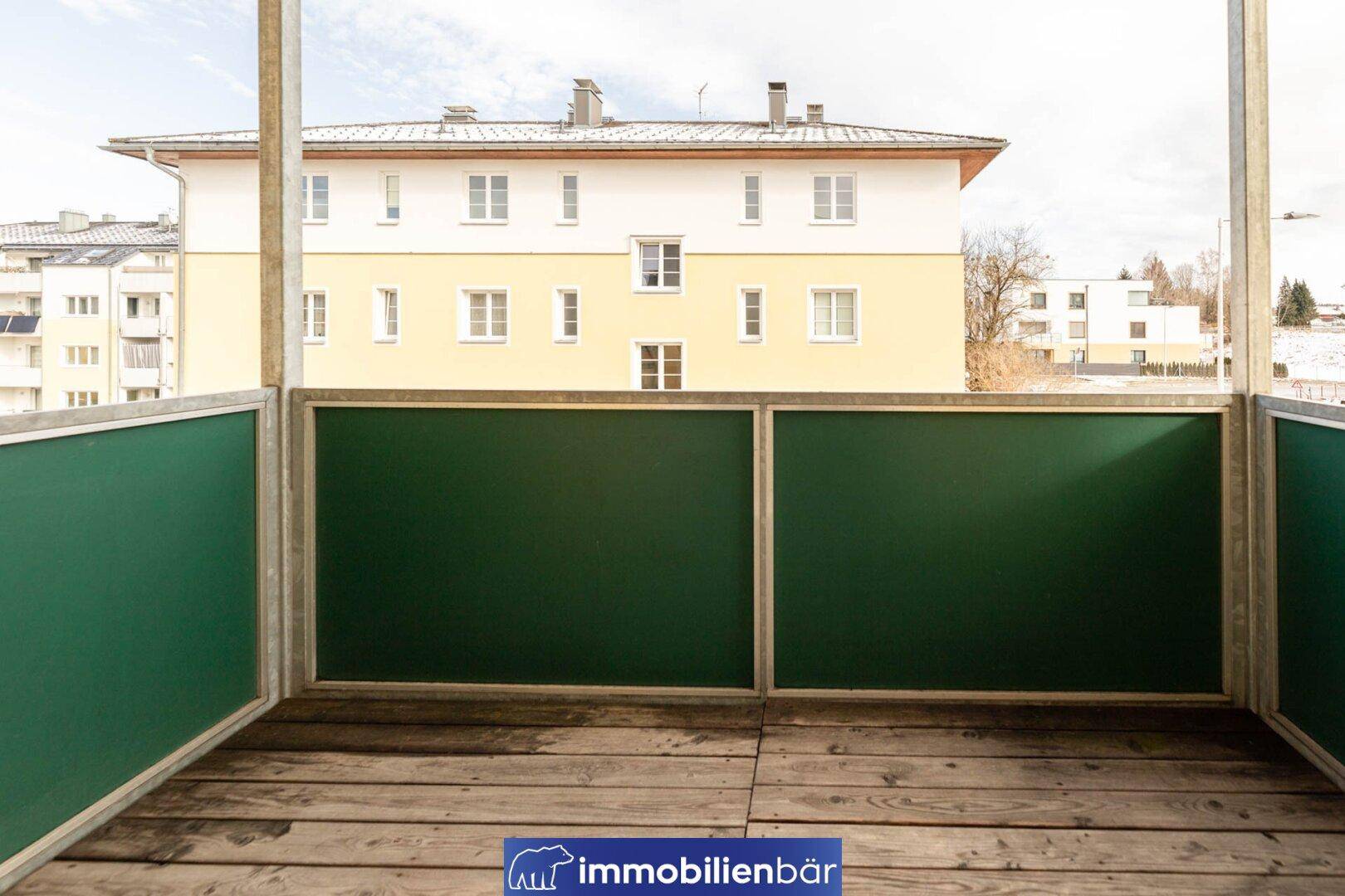 Balkon mit Holzboden und grünen Brüstungen, bietet Blick auf die umliegenden Gebäude.