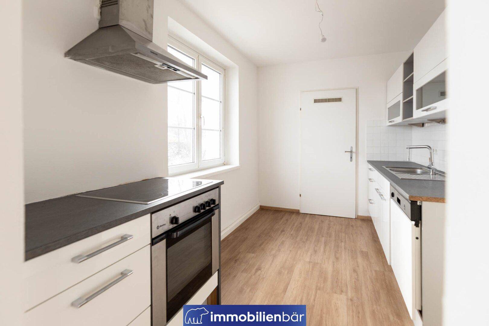 Moderne Küche mit weißen Schränken, dunklen Arbeitsplatten, Backofen und Induktionskochfeld.
