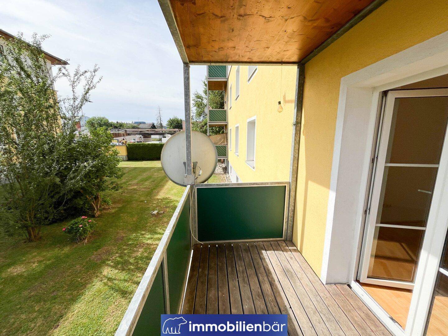 Balkon mit Holzboden und Blick auf den grünen Gartenbereich der Wohnanlage.