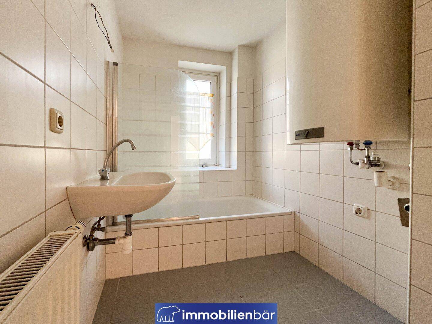 Gefliestes Badezimmer mit Badewanne, Waschbecken und Fenster für Tageslicht.