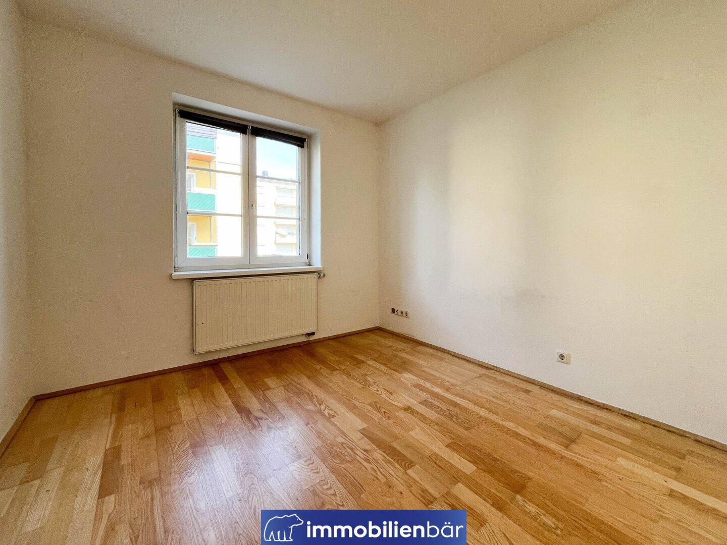 Freundliches Zimmer mit Holzparkett und einem Fenster, das viel natürliches Licht bietet.