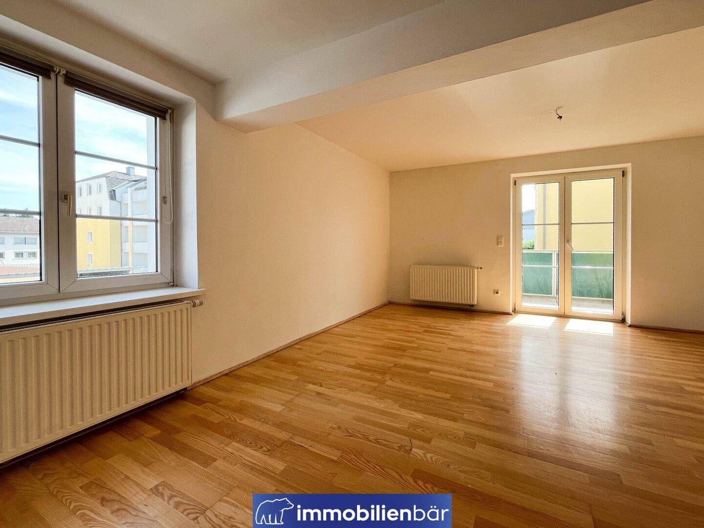 Heller Wohnbereich mit Parkettboden und Zugang zu einem Balkon oder einer Terrasse.