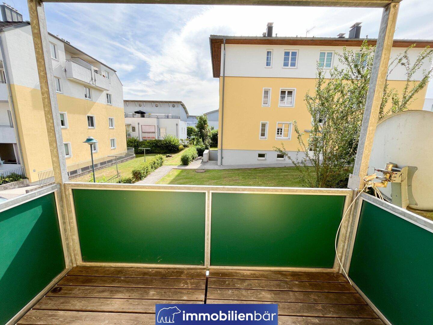 Kleiner Balkon mit Holzboden und Blick auf die grüne Umgebung des Gebäudes.