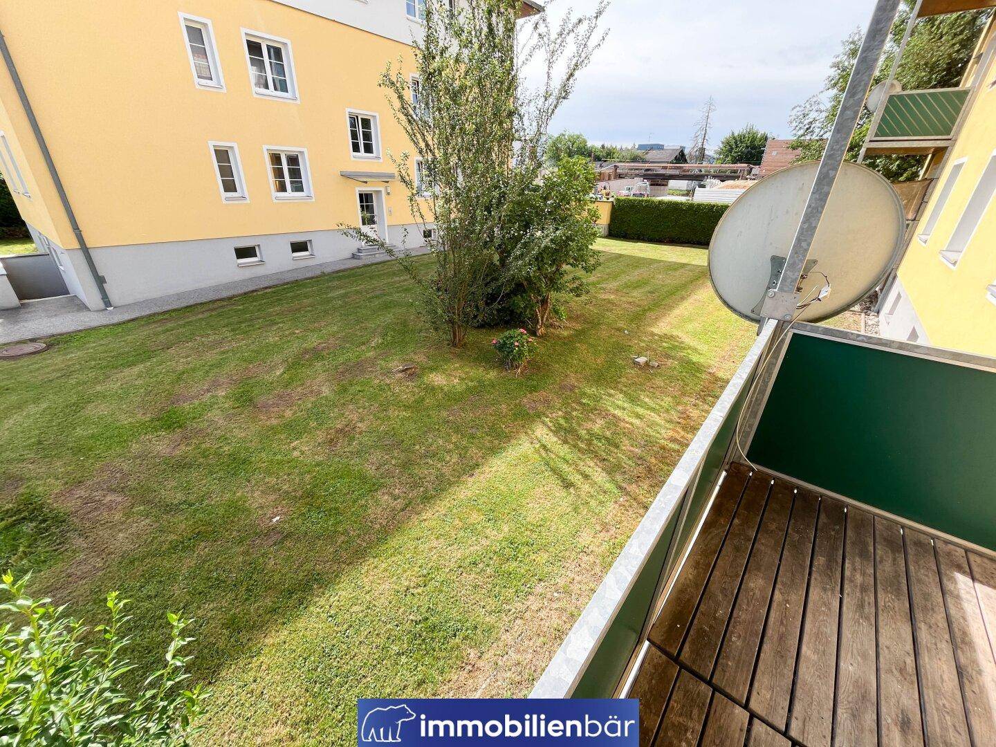Balkon mit Holzboden und weitem Blick über die grüne Rasenfläche der Anlage.