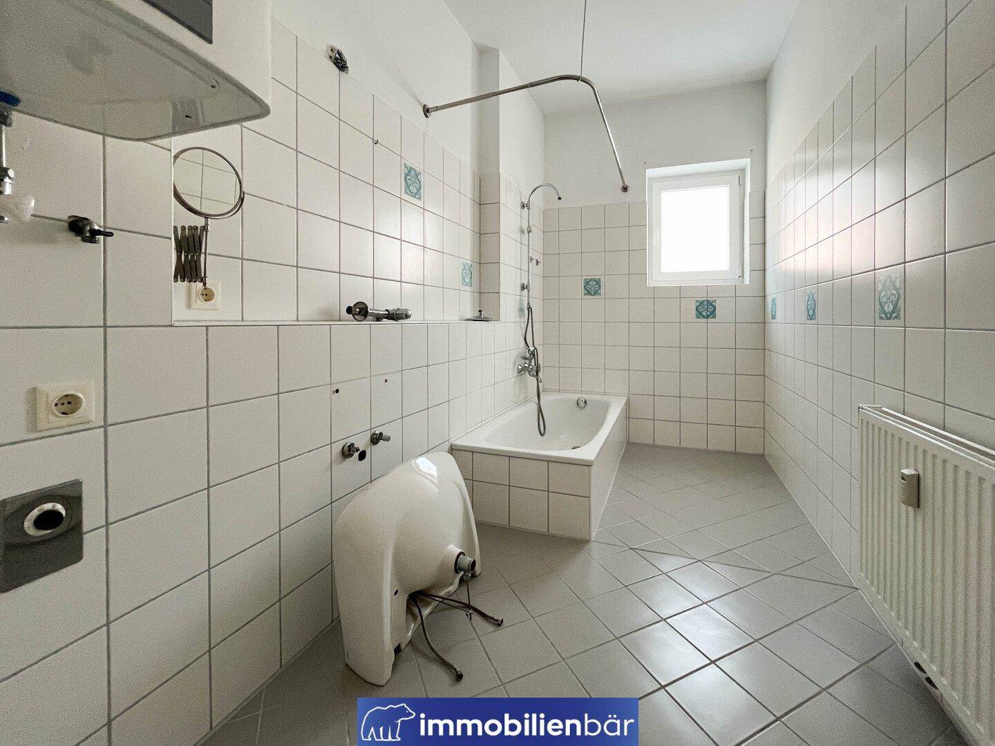 Gefliestes Badezimmer mit Badewanne, Fenster und Heizkörper, bereit für eine Modernisierung.