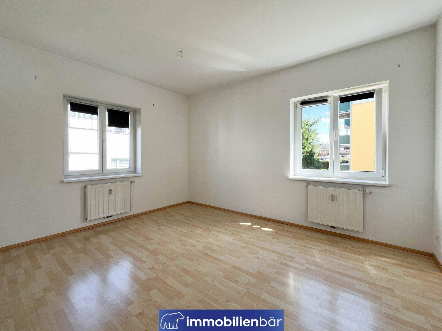 Helles Zimmer mit zwei Fenstern und Parkettboden, bietet viel natürliches Licht und eine angenehme Atmosphäre.