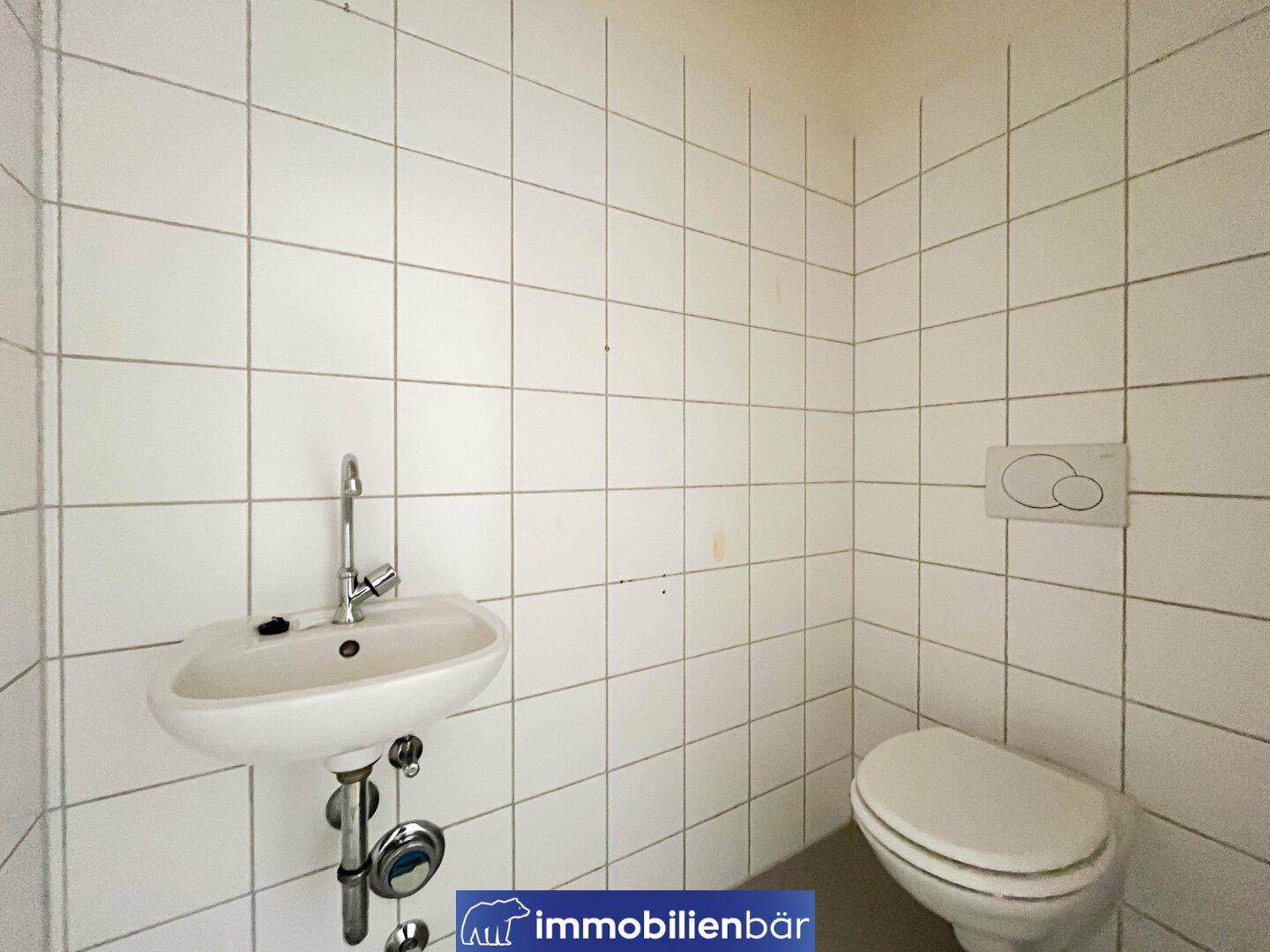Kleines Gäste-WC mit weißen Fliesen, wandhängendem WC und einem Waschbecken.