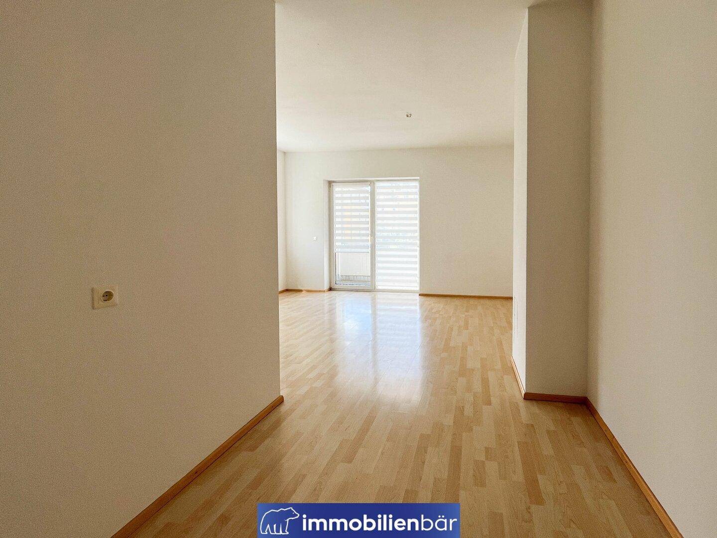 Geräumiger Wohnbereich mit hellem Parkettboden und Zugang zu einem sonnigen Balkon.