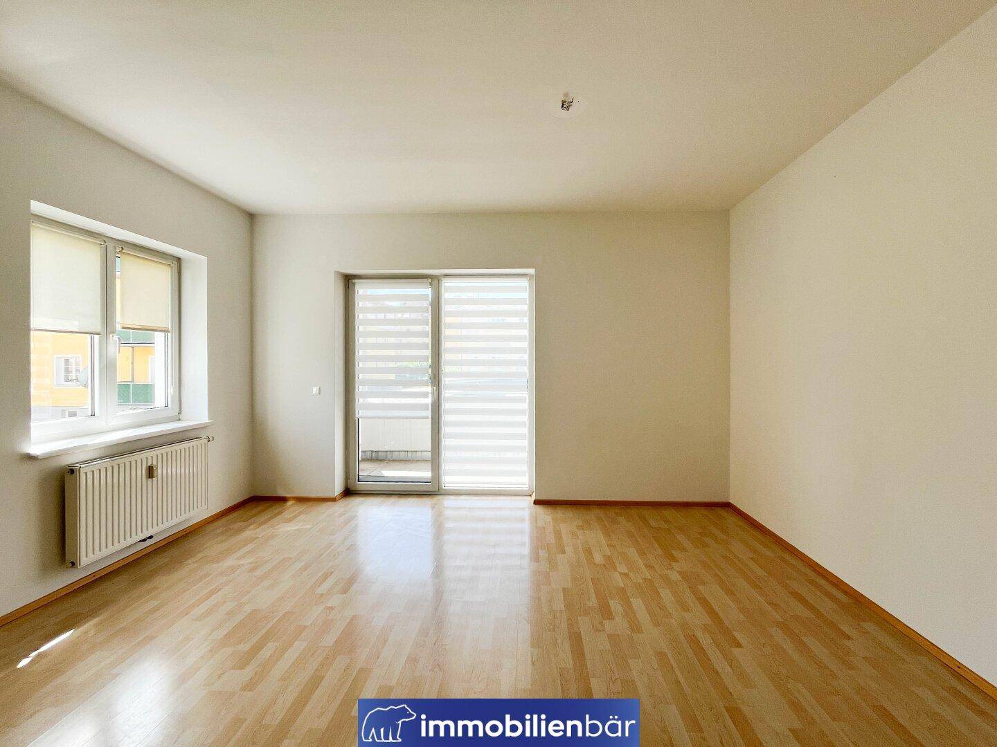 Geräumiges Zimmer mit hellem Parkettboden und großem Schiebetürzugang zum Balkon.