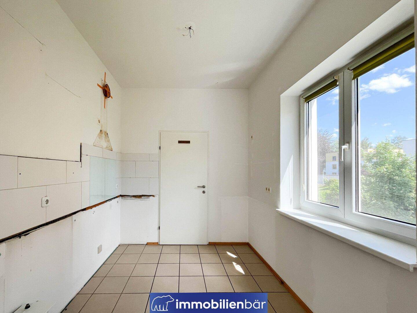 Leere Küche mit Fliesenboden und Fenster, bereit für die Installation einer neuen Einbauküche.