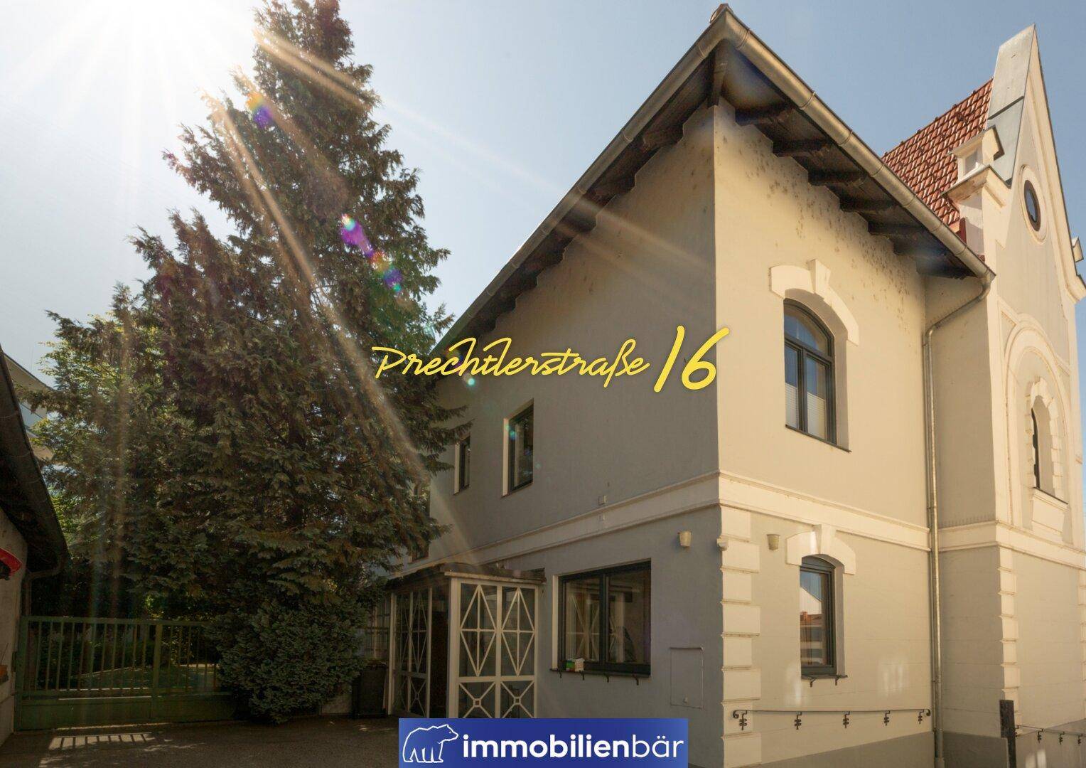 Historisches Gebäude mit klassischer Architektur, hellgrauer Fassade und einem kleinen verglasten Eingangsbereich.