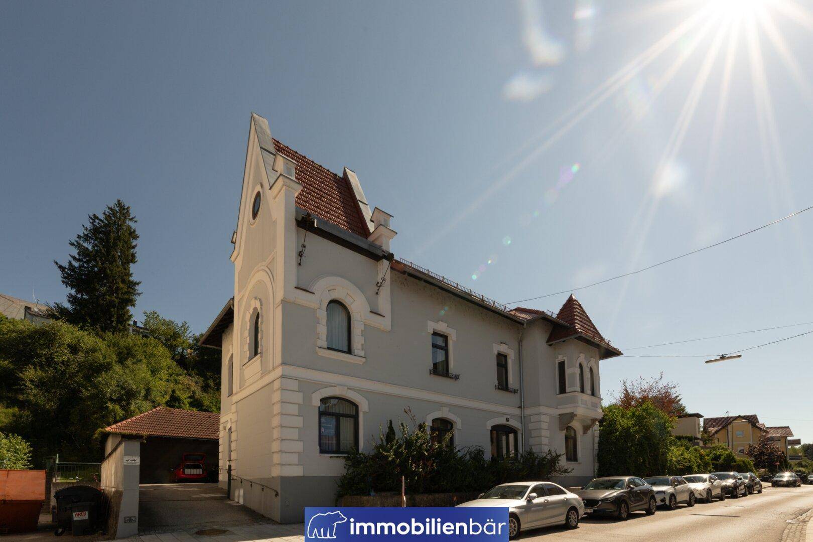 Historisches Gebäude mit markanter Architektur, hellgrauer Fassade und parkenden Autos an der Straße.