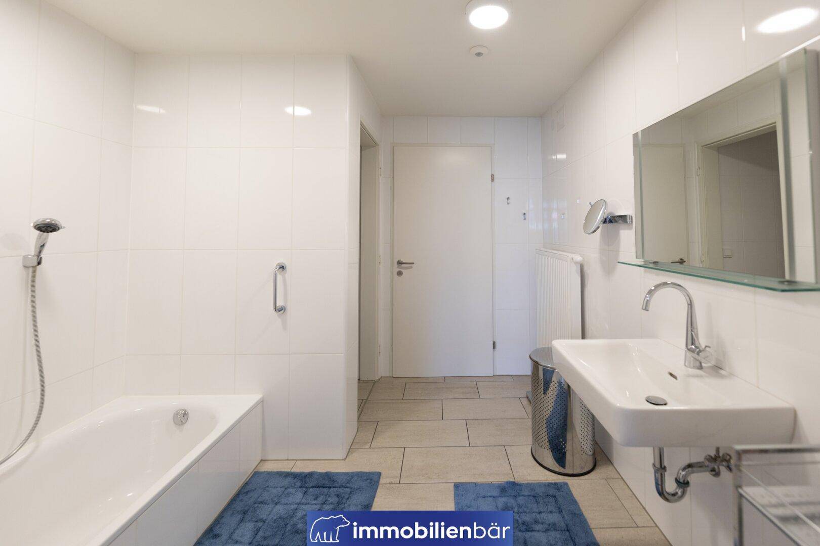 Modernes Badezimmer mit weißen Fliesen, Badewanne mit Duschfunktion und einem einzelnen Waschbecken.