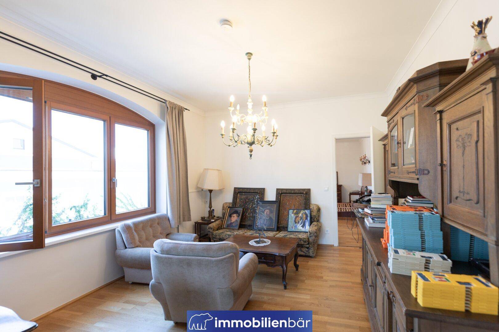Gemütliches Wohnzimmer mit traditionellen Möbeln, einem großen Fenster und einem eleganten Kronleuchter.